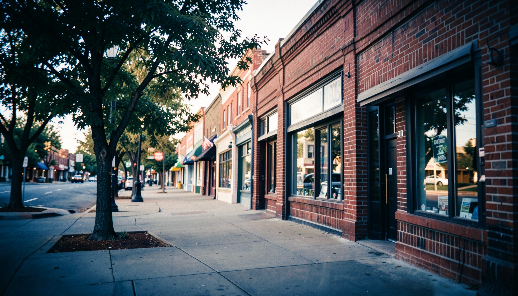 Warm-toned image of a welcoming Kansas main street with brick storefronts and trees lining the sidewalk